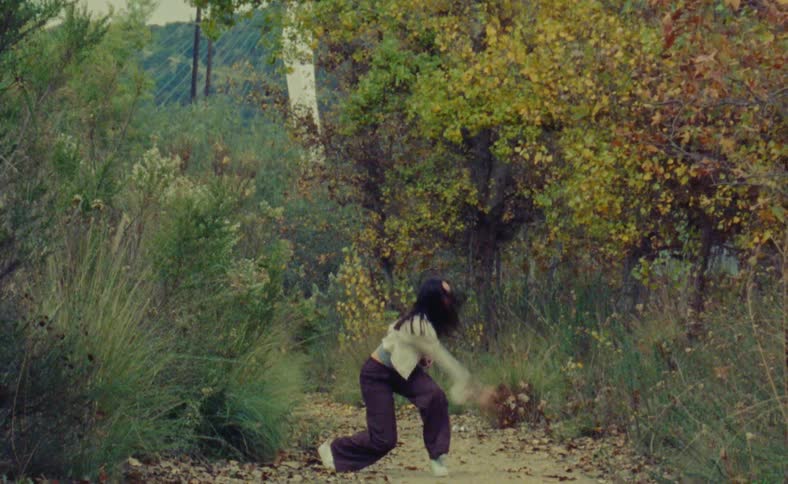 A woman is dancing outdoors surrounded by nature