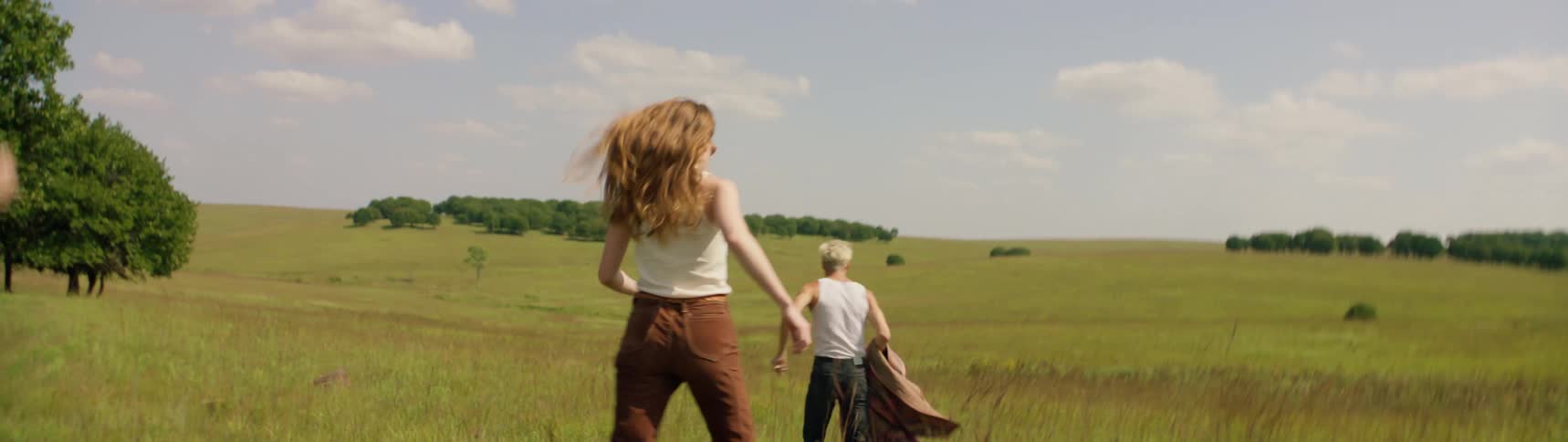 A small group of young adults are running outdoors in a large rural field carrying a blanket during the daytime