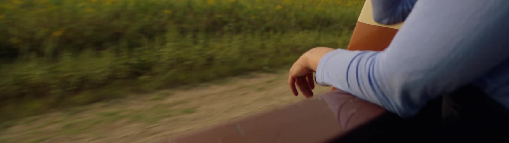 A woman is sitting in the back of a pickup truck with her arms over the side as it travels on a rural road
