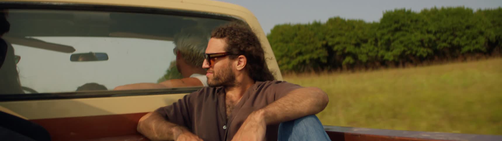 Man sits on the back of a pickup truck driving on the countryside at daytime