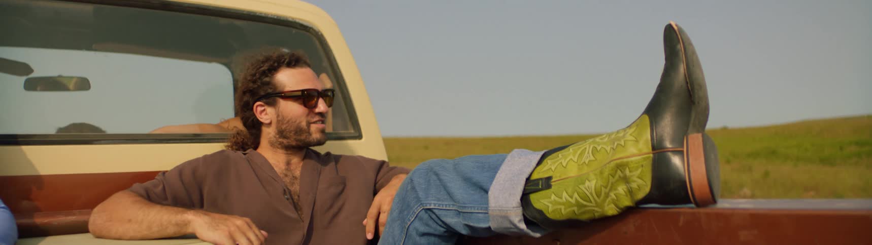 A man is riding in the back of a pickup truck with his foot propped up on the side