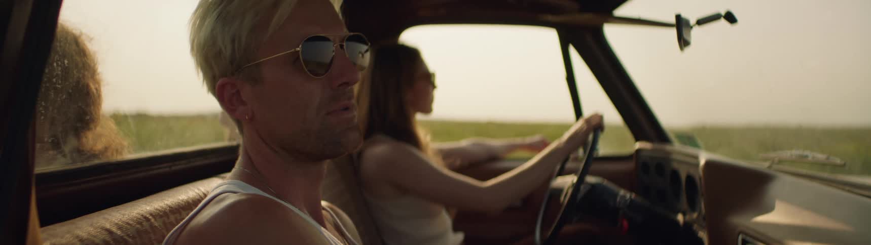 A group of friends ride in a pickup truck past a field