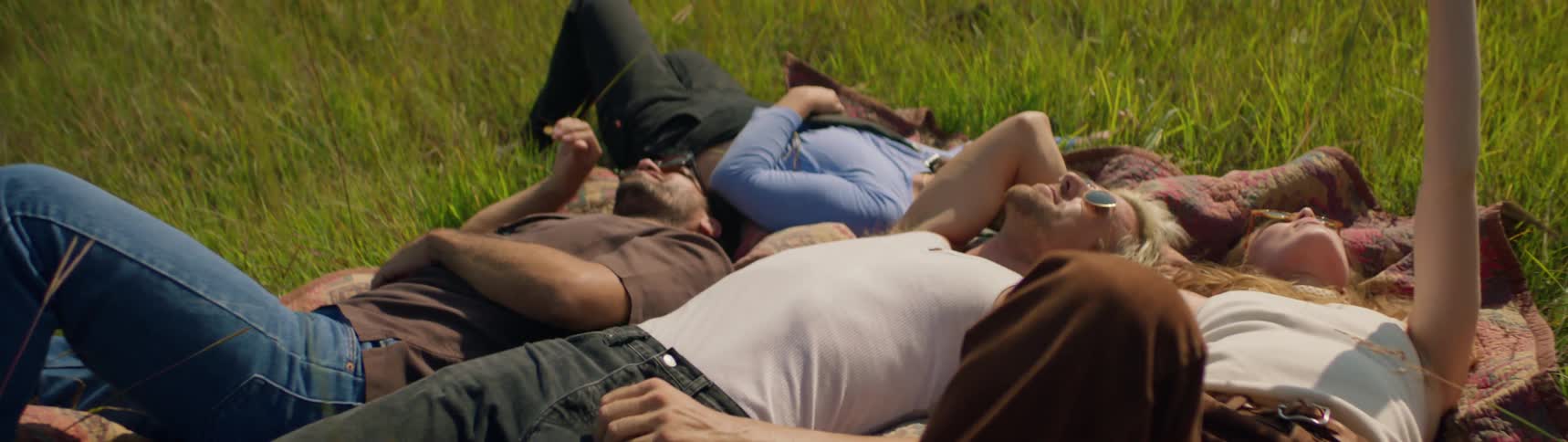 Friends lie close together on blanket in field