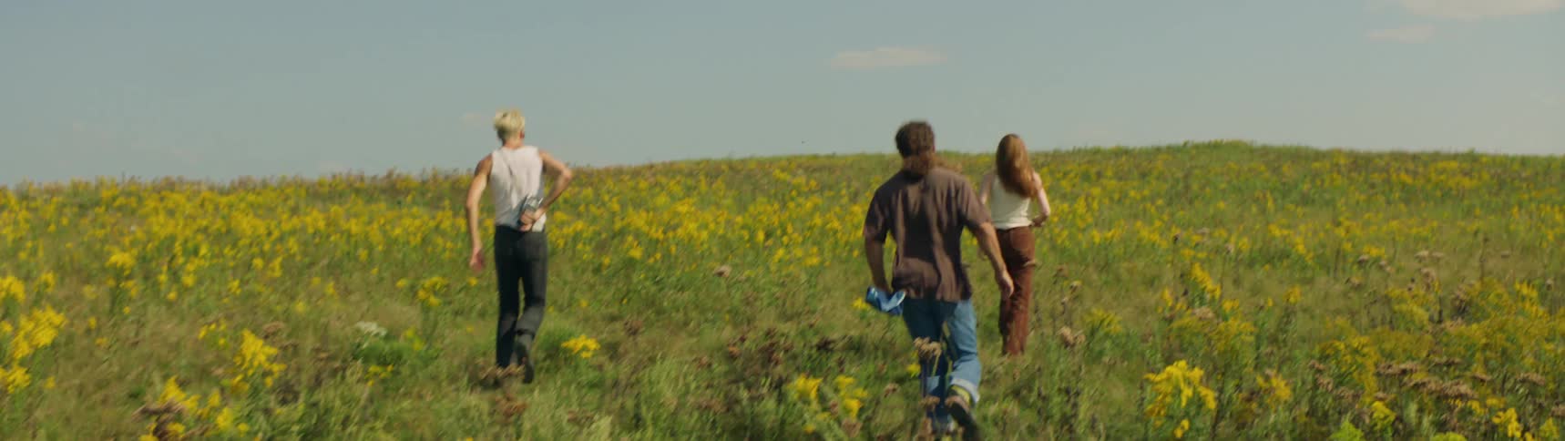 Group of friends run across flower strewn meadow