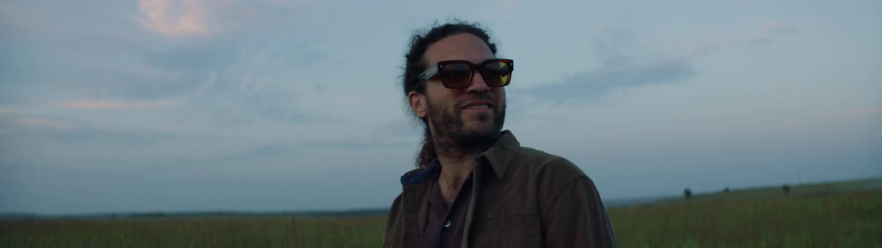 A man is standing outdoors in a rural area and smiling
