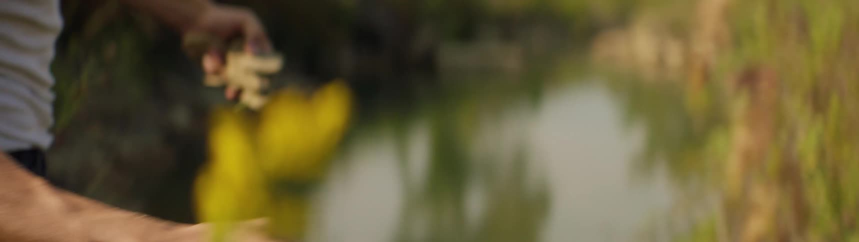 A man is outdoors skipping rocks onto a pond during the day
