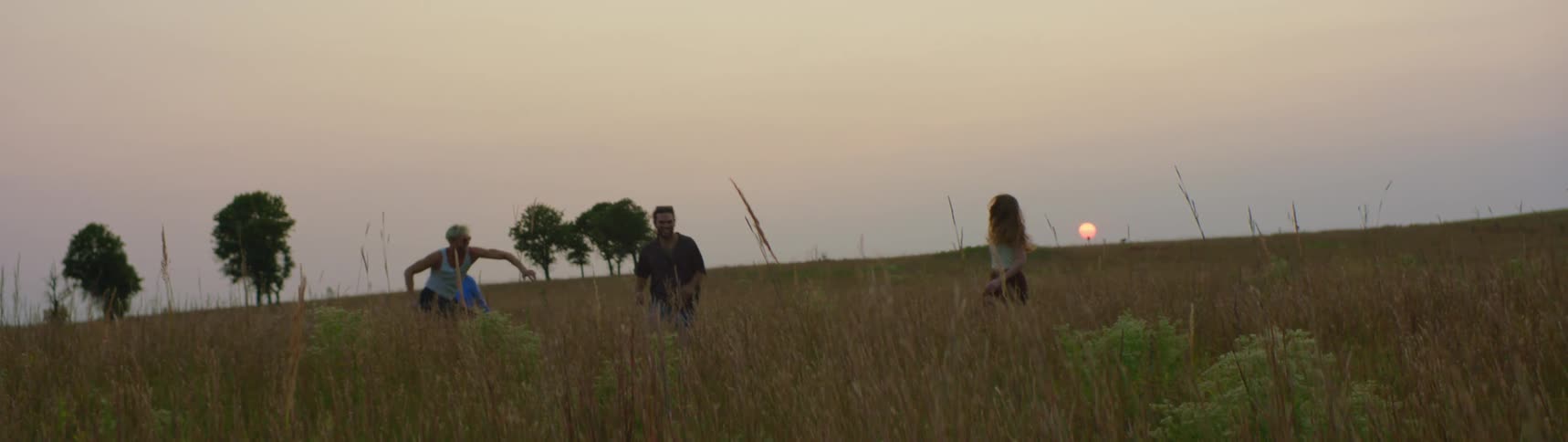 Friends play in fieldas sun sits above the horizon in the background