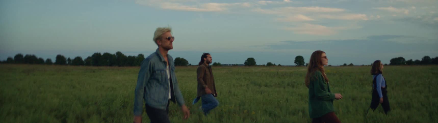 A group of four people are walking through a grass field