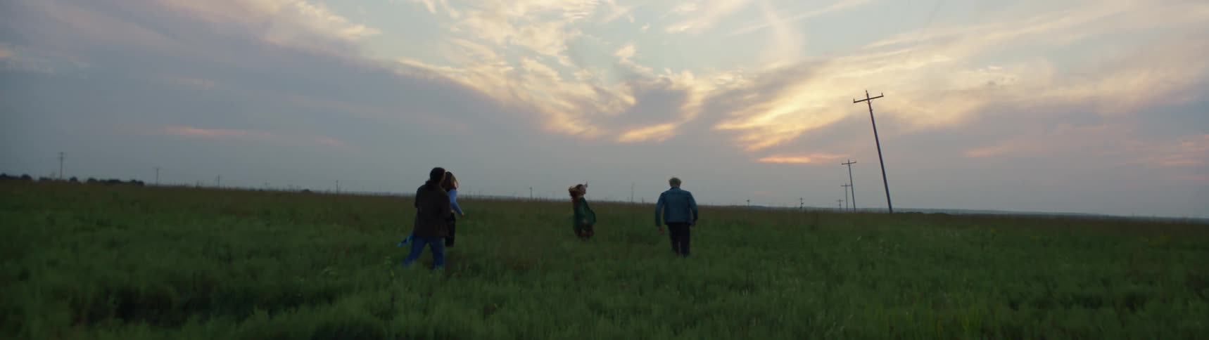 Four teenagers walk through a field together
