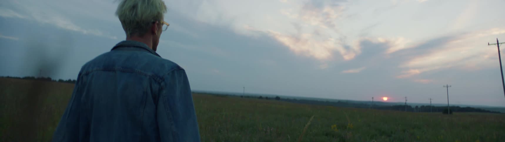 A man is walking through a field in a rural area at dusk