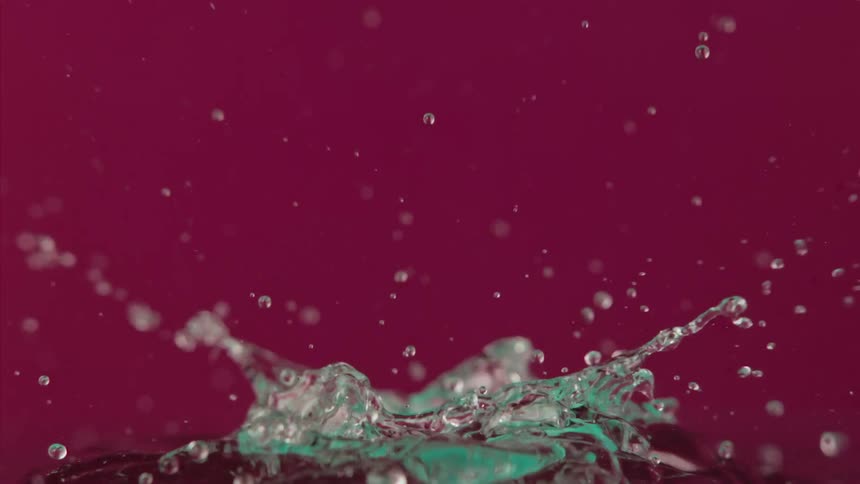 A clear sphere falls down in a red environment and splashes with liquid flying and droplets floating in the air as they fall