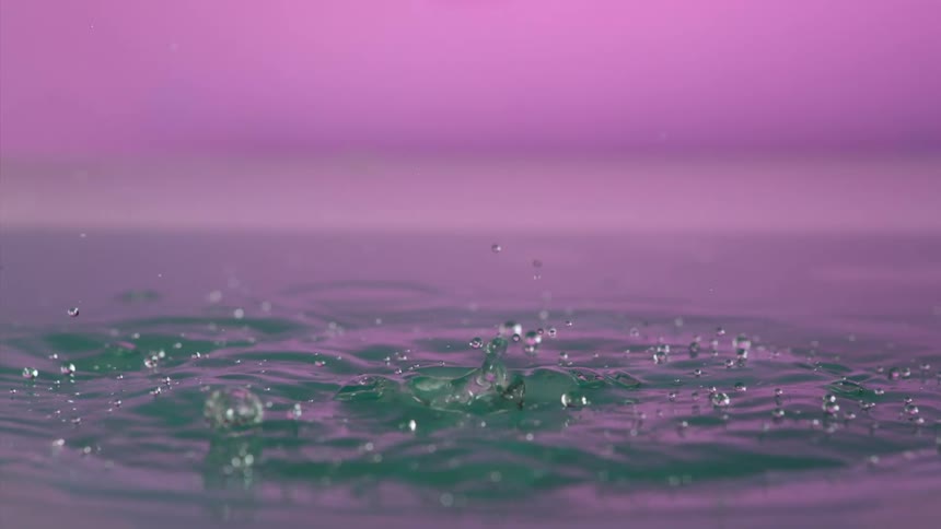 Clear spheres fall down in a pink environment and splash with liquid flying and droplets floating in the air as they fall