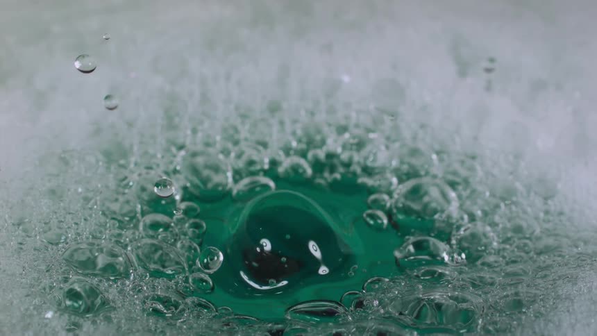 A close view of water dropping into a foamy and bubbly liquid in the daytime