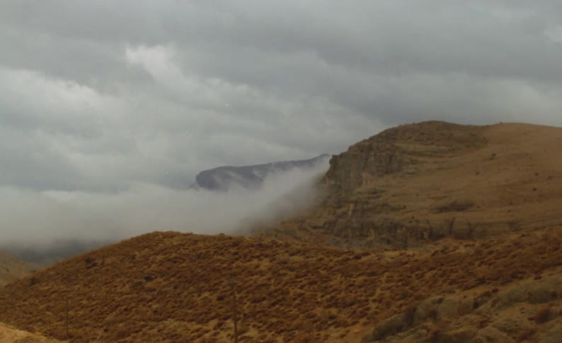 Dense fog covers portions of hill and mountain on overcast day