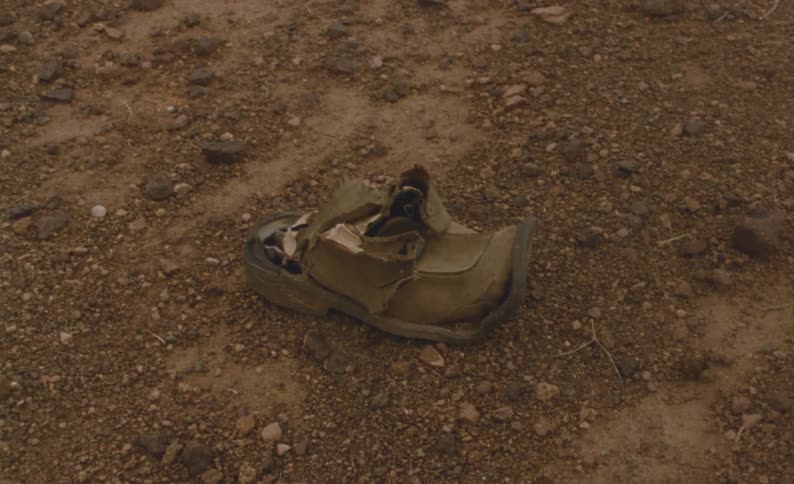 An old shoe is sitting on the ground among dirt and stones