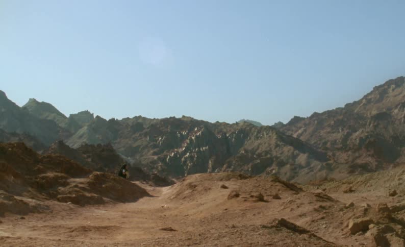 A desert mountain range against a blue sky and a person in the distance
