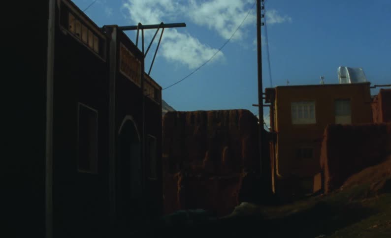 Shadow covers a back alley with surrounding buildings under a blue sky with a few clouds