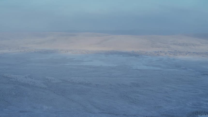 Snow and ice covered landscape stretches from lake to mountains on the horizon