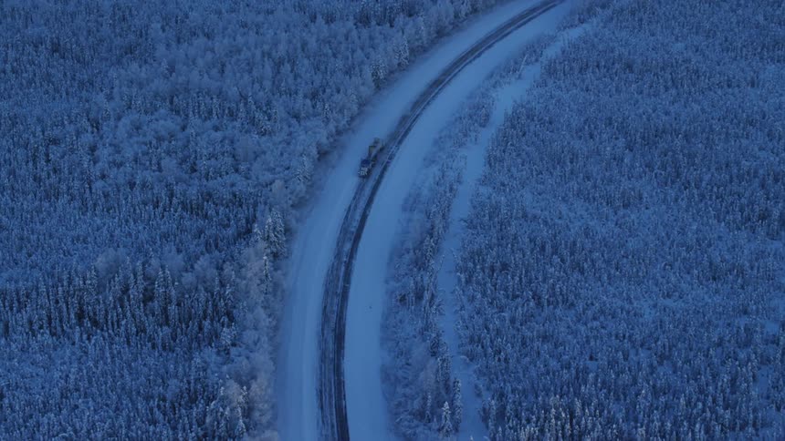 A semi drives down a curvy snow covered road through the forest