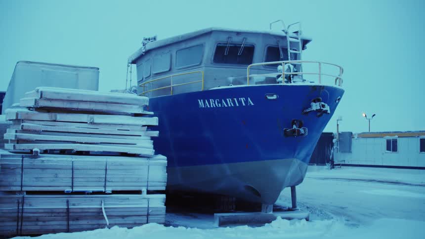 A boat sits parked in a lot next to a stack of pallets