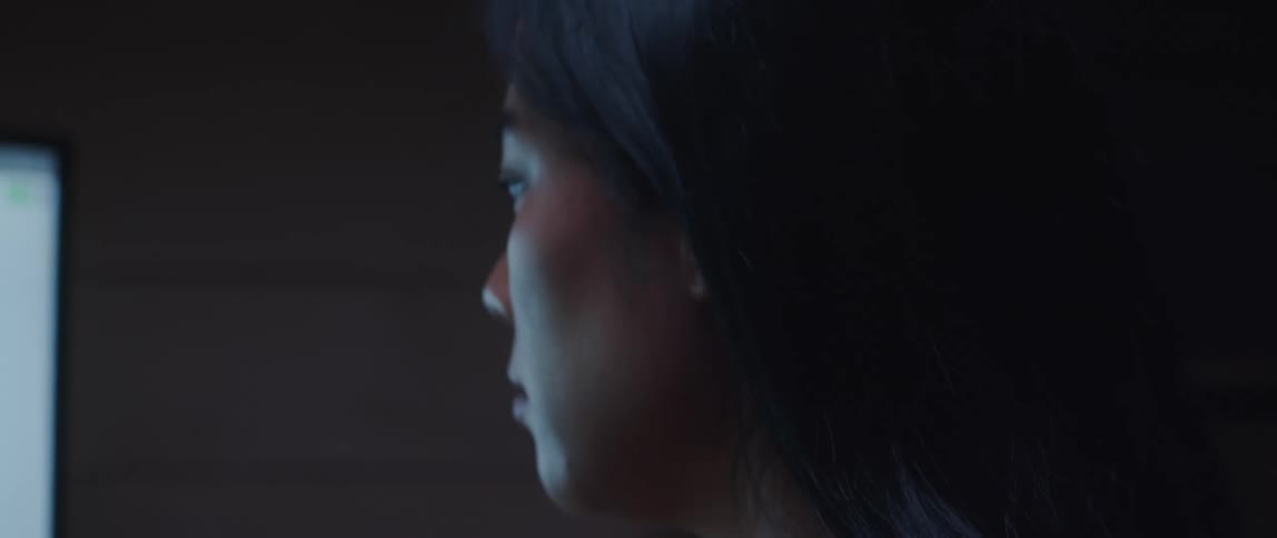 A young asian woman looking up in thoughts then looking back at a screen in front of her