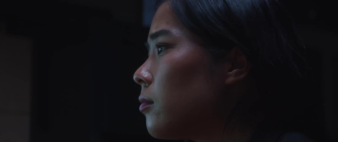 Light from a computer monitor shines on a woman's face as she looks up and down squinting her eyes