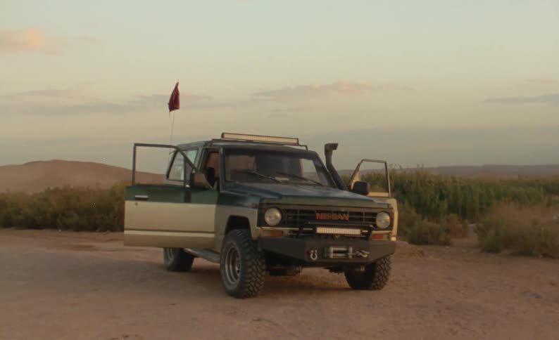A vehicle sits parked with its doors open in a dirt field