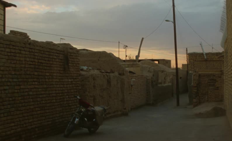 A motorcycle sits parked in an alley along a brick wall