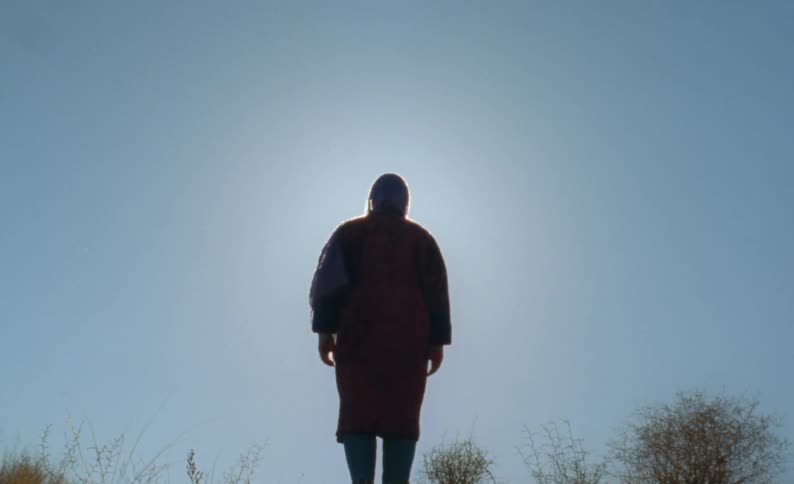 A woman stands in a field and looks off in to the distance