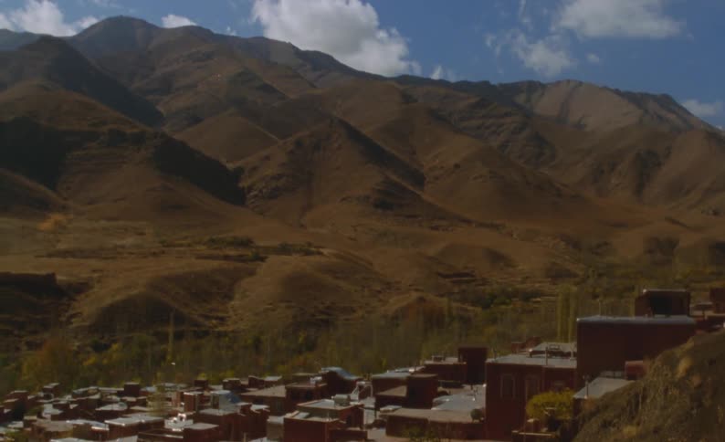 Field separates town from foot hills of mountains under a cloudy sky