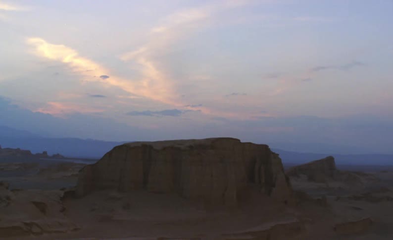 A desert rock formation against a dusk sky with mountains in the background