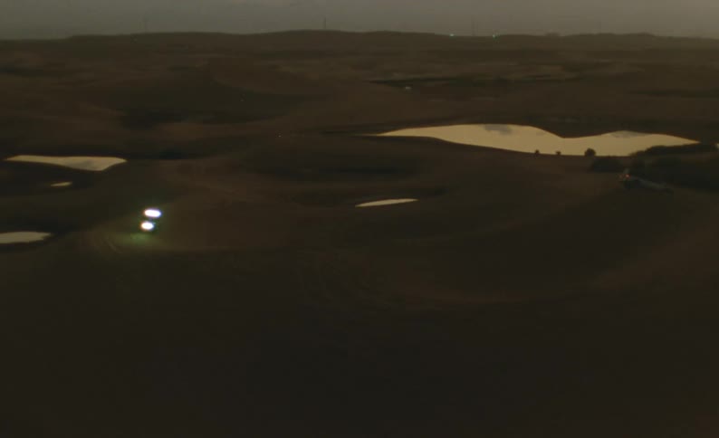 An off road vehicle drives along dunes in the desert