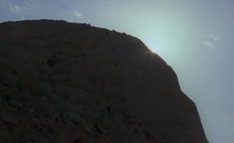 Rays of sunlight shine over the edge of a mountain cliff