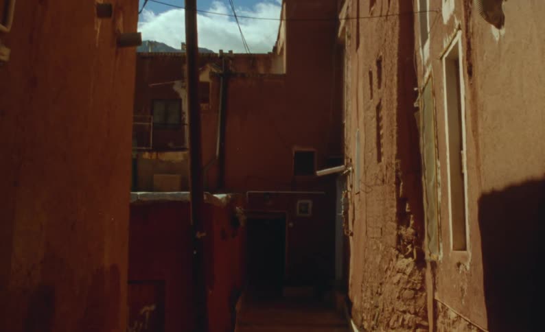The sun shines on dilapidated buildings and there is an alley leading to an open door