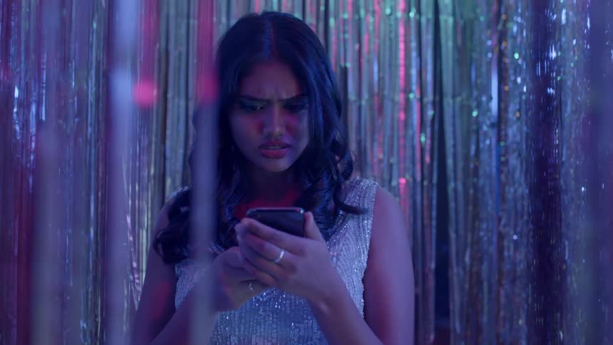 A woman standing looking at her phone confused and then angrily then speaking at someone