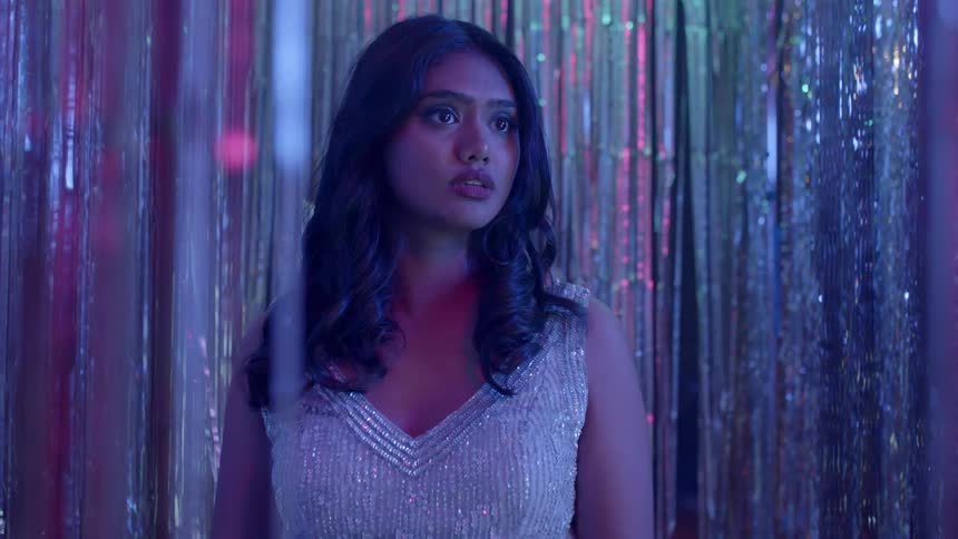 Worried woman with dark wavy hair and silver glitter dress looks into space in a night club
