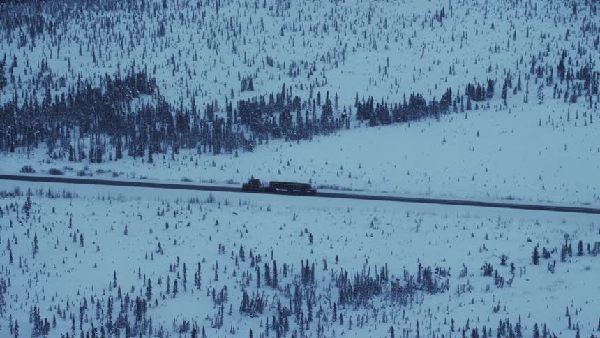An aerial view of a truck driving through a frozen forest