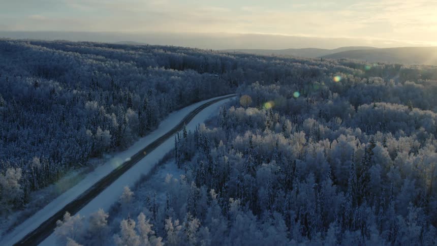 An aerial view of a house next to a snowy forest in a rural area