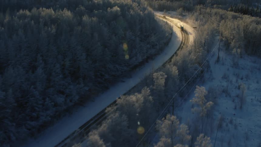 The sun shines brightly over a mountain as a train travels through a snow covered forest on a winter day