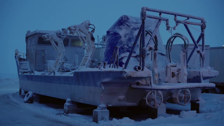 A snow covered boat is sitting on bricks in a parking lot next to trucks