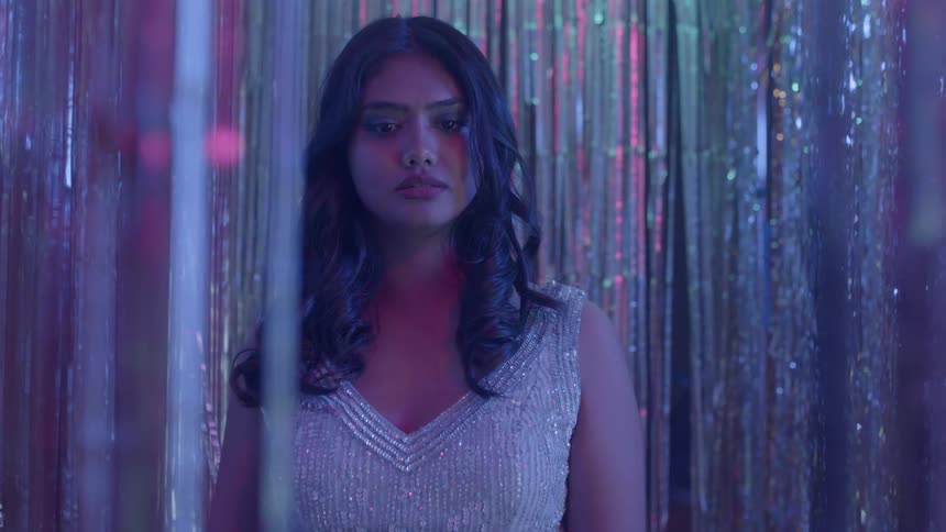 Woman with dark wavy hair and glitter dress stands and looks around in night club