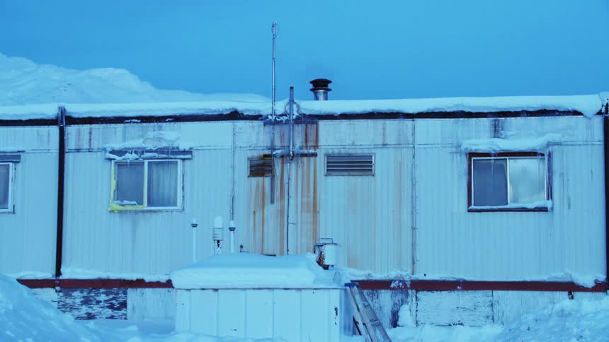 A long white building that is snow covered with pipes running down the backside