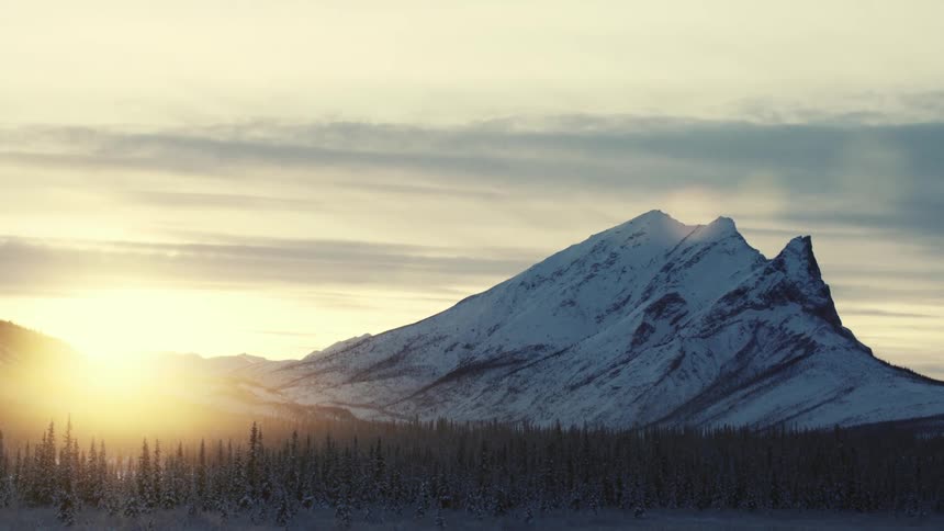 Sunlight coming up over the mountains showing off a tall snow covered mountain