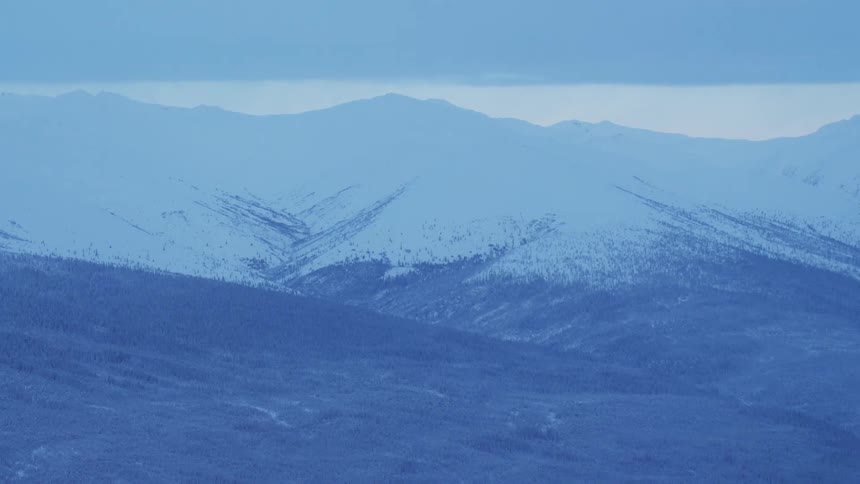 An aerial view of a snow covered peak giving way to a valley