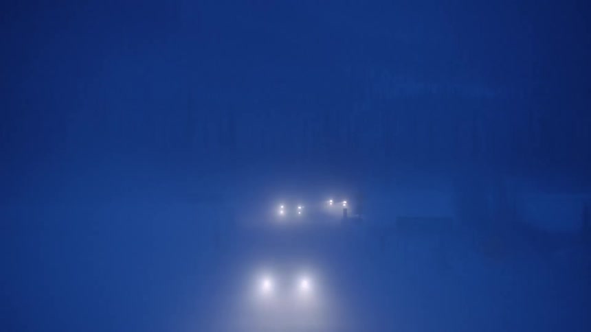 Three cars driving on a road at nights with their headlights on in fog and snow
