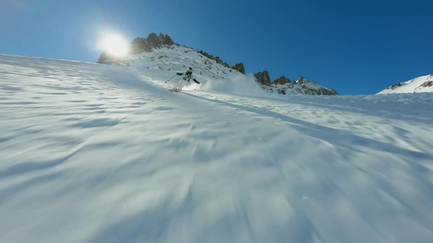 A person skiing down a snowy mountain with rocky peaks in the background