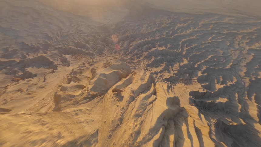 Drone shot rushing down the slopes of a roc formation in the desert at sunset
