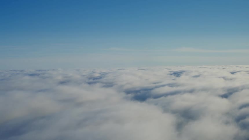 Flying above the thick white clouds among a clear blue sky