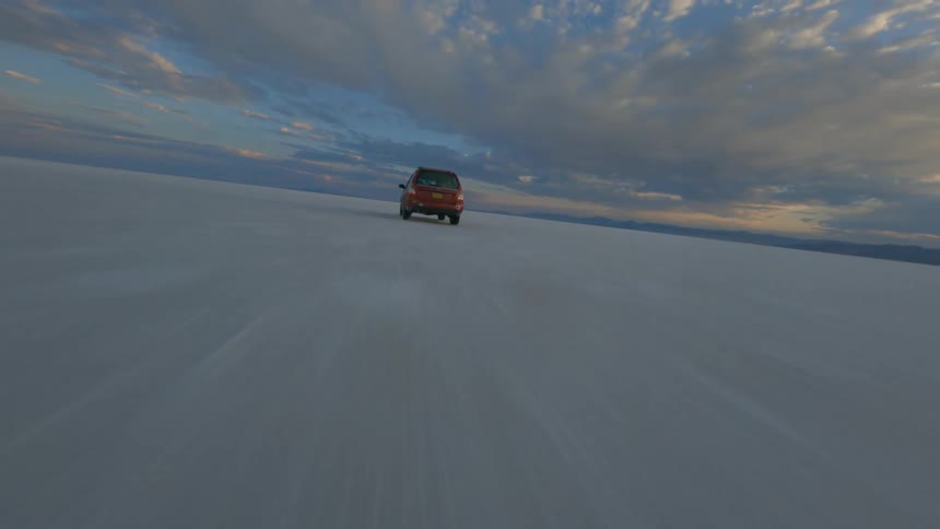 Aerial shot of a red suv driving through a flat desert area at dusk