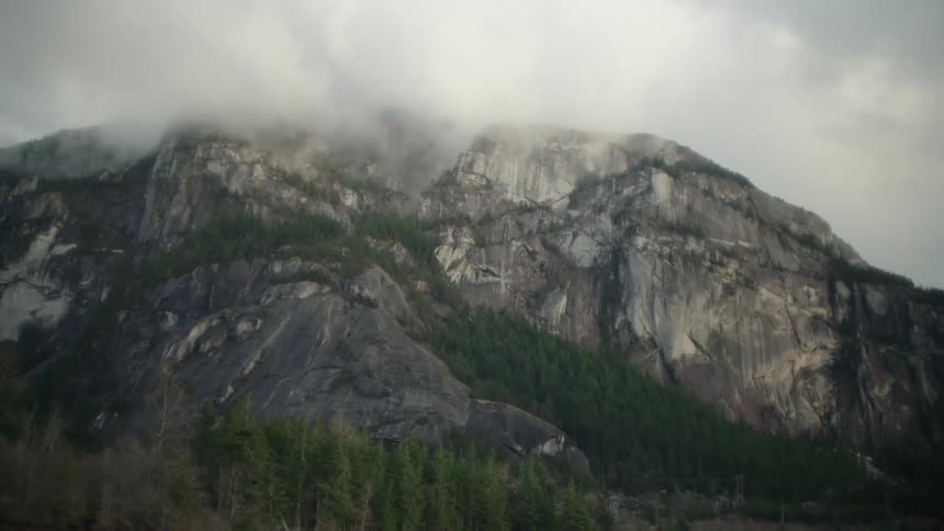 Forest hugs slope and base of mountain as clouds obscure the summit